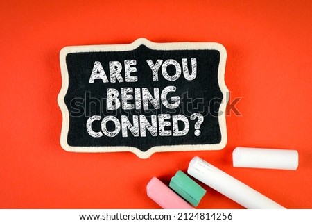 Are You Being Conned. Miniature chalk board with chalk pieces on red background.