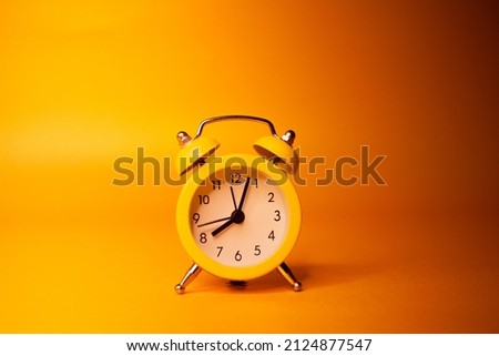 Little analog alarm clock on a yellow background
