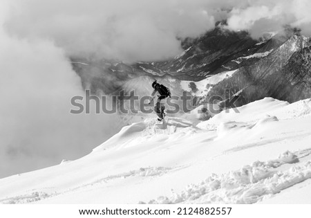 Snowboarder on snowy off-piste slope, high winter mountains in fog. Caucasus Mountains, Georgia, region Gudauri. Black and white toned image. Royalty-Free Stock Photo #2124882557