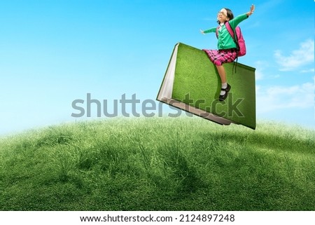 Asian little girl with eyeglasses sitting on a flying book. World Book Day Royalty-Free Stock Photo #2124897248