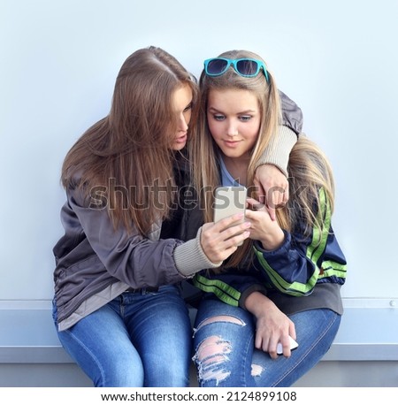 two smiling girls posing on the city street ,taking pictures ,using smartphone