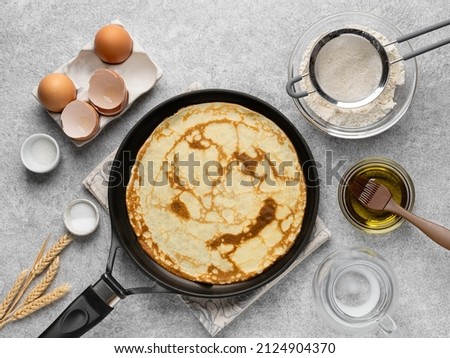 Thin pancakes (crepes, russian blini). Step by step cooking process. Frying crepe (pancake) on black skillet. Maslenitsa concept. Top view. Cooking ingredients. Grey background. Royalty-Free Stock Photo #2124904370