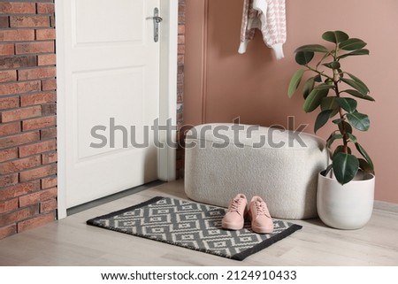 Hallway interior with beautiful houseplant, soft ottoman and door mat on floor near entrance Royalty-Free Stock Photo #2124910433