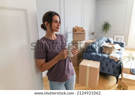Beautiful woman holding a cup of coffee in her hands making break from moving in while proudly looking around the new apartment she bought Royalty-Free Stock Photo #2124921062