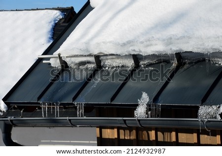 galvanized metal roof in the mountains with a bar against the rapid sliding of snow. If snow and ice quickly fall on people under the roof, they will be injured or dead. slows down the avalanche Royalty-Free Stock Photo #2124932987