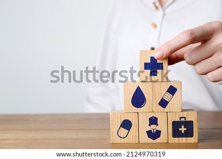 Woman building pyramid of cubes with different icons on wooden table against light background, closeup. Insurance concept