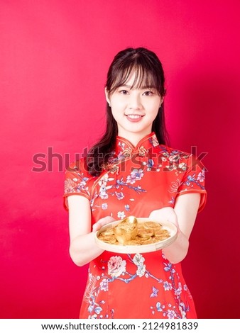 Happy asian young woman wearing traditional cheongsam qipao dress showing Gold ingot for celebrating chinese new year on red background.