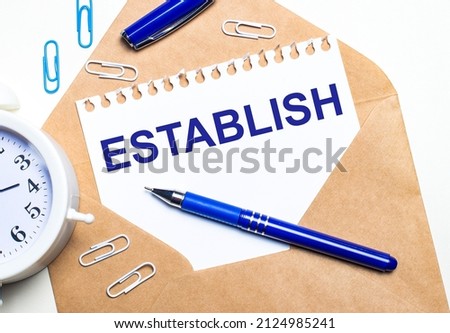 On a light background, a craft envelope, an alarm clock, paper clips, a blue pen and a sheet of paper with the text ESTABLISH