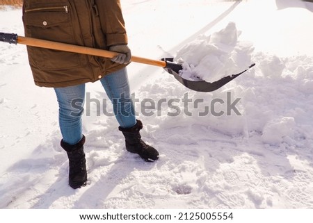 Snow removal in winter. A woman cleans the snow with a shovel in the local area.