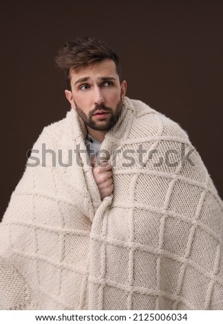 Man wrapped in blanket suffering from fever on brown background. Cold symptoms Royalty-Free Stock Photo #2125006034
