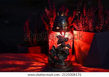 Grave lantern with burning candle on stone surface at night