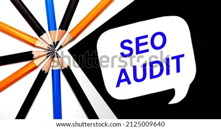 On a light background, multi-colored pencils and on a black background a white card with the text SEO AUDIT