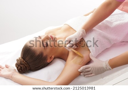 Beautician is removing hair from young female armpits with hot wax. Woman has a beauty treament procedure. Depilation, epilation, skin and health care concepts. Royalty-Free Stock Photo #2125013981