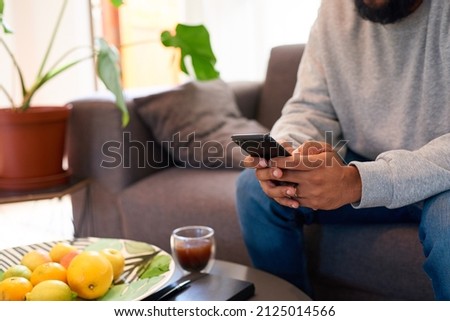 A man's hands typing on a smart phone while he sits on the couch