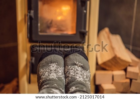 Feet in winter socks are heated by the fireplace. Rest in the mountains in Glamping. Cozy fireplace in a mountain house Royalty-Free Stock Photo #2125017014