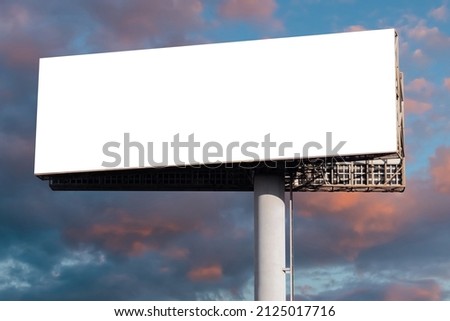 Mock up - blank wide white billboard against warm sunset sky with clouds. Consumerism, white screen, template, copy space and mockup concept