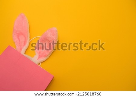 Easter sale, pink bag with pink bunny ears on yellow background, space for text, easter card.