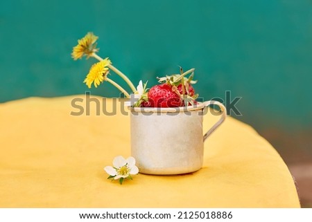 Strawberries and dandelions in a metal aluminum travel mug. Green and yellow spring background. Cottagecore aesthetics concept, trendy shadows background. Copy space. High quality photo