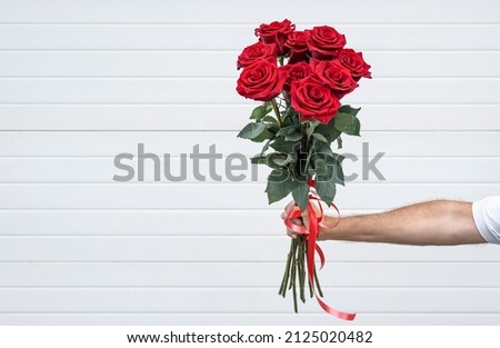 Bouquet of flowers in hand on a light background. Gentleman with a bouquet of red roses.