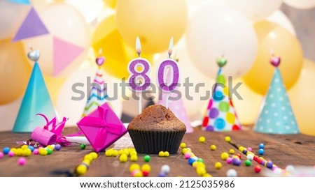 Happy birthday with a number of candles for eighty years on the background of balloons. A festive muffin with burning candles and a pink gift box for a woman. Happy birthday for 80 years