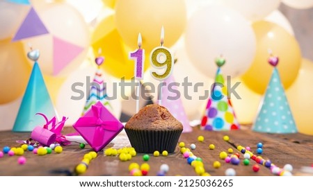 Happy birthday with a number of candles for nineteen years old against the background of balloons. A festive muffin with burning candles and a pink gift box for a girl. Happy birthday for 19 years old