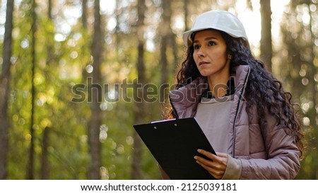 Millennial female technician ecologist looking up at treetops, Young indian woman in hardhat with clipboard taking measures checking trees. Forestry engineer in park. Supervising wildlife sanctuary Royalty-Free Stock Photo #2125039181
