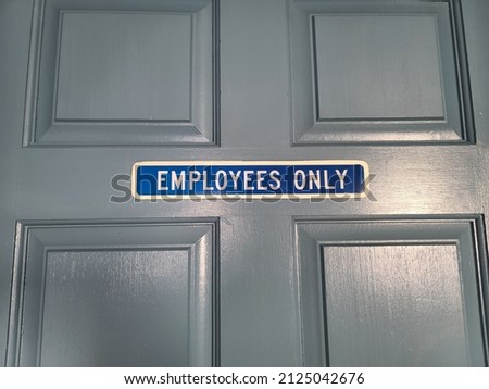 A sign that indicates employees only. The sign is hung on a door that is painted blue gray.