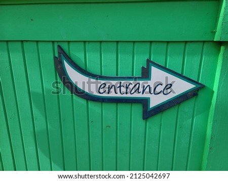 An entrance sign attached to a green wall. The word entrance is written on a sign in the shape of an arrow pointing in the direction of the entrance.