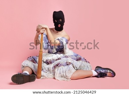 Defense. Comic portrait of young funny girl in image of medieval royal person in renaissance style dress and black balaclava isolated on pink background. Comparison of eras, beauty, humor, art