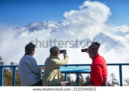 Three travellers take picture by mobile and camera of snow peaks in Himalayas. Beautiful view of South Annapurna in Dobato in Nepal 2021.