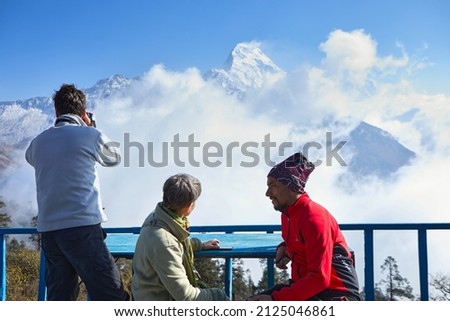 Three travellers take picture by mobile and camera of snow peaks in Himalayas. Beautiful view of South Annapurna in Dobato in Nepal 2021.