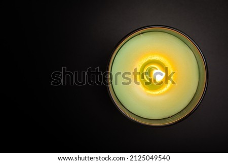 Burning aroma candle in glass on black background top view. Green aromatic wax candle with copy space. Candlelight close up Royalty-Free Stock Photo #2125049540