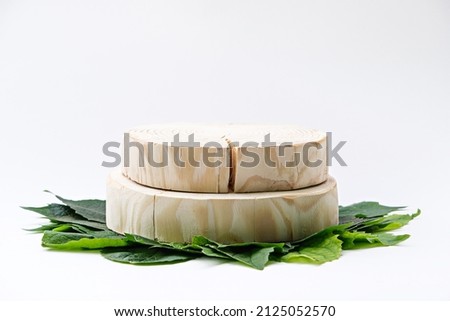 two round wooden podium on green leaves on white background, sawn cut