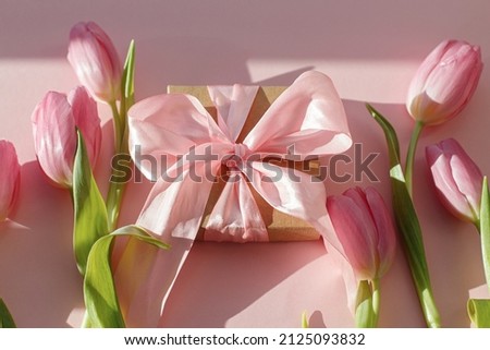 Pink tulips and gift box in sunlight on pink background. Happy womens day. 8 march. Happy Mothers day. Creative stylish greeting card. Modern image