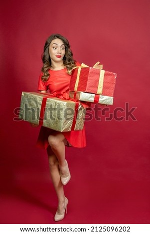 Surprised brunette woman with a gift in red dress on a red background.