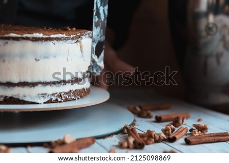 culinary, baking and cooking food concept - woman making layer cake and spreading topping cream on kitchen at home