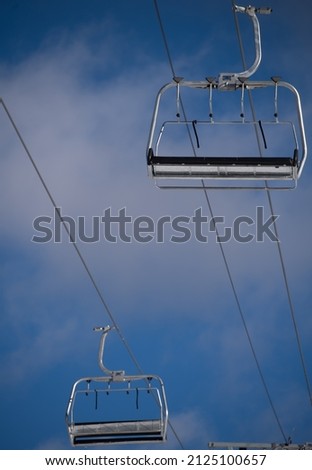 two isolated silver metal empty chairs on ski chair lift hanging from large heavy duty industrial cable at ski resort clear day blue skies above in background vertical format room for type content 
