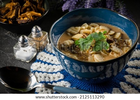 Mushrooms soup with noodles on black table.