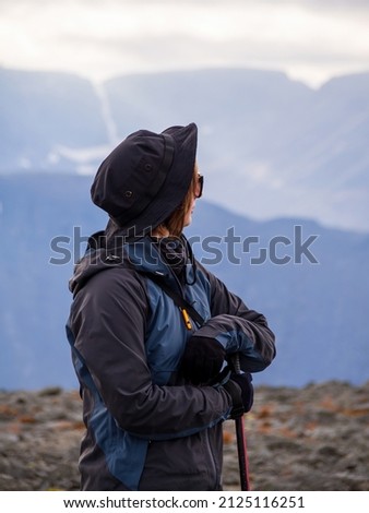 A woman in a hat on a mountain slope looks through binoculars in autumn against the backdrop of a lake and mountains. view from the back. photo