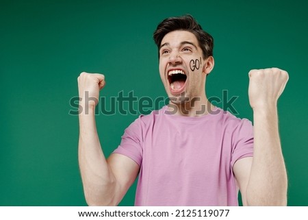 Young fun crazy happy european man fan supporter wears basic pink t-shirt cheer up support football sport team watch tv live stream scream clench fists isolated on dark green color background studio Royalty-Free Stock Photo #2125119077
