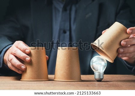 Man is playing a shell game by paper cups and reveals the right one that glowing light bulb is hiding, tips and tricks, good choice answer, find a creative idea