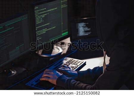 Hacker in front of computer. view from shoulder. hacker in the hood typing text
