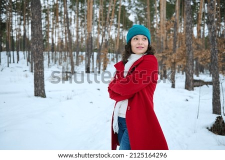 Beautiful serene dark-haired woman in a red warm coat walks along a snowy forest path, enjoys a weekend outdoors on a beautiful cold winter day. Concept of winter active pastime and leisure activity Royalty-Free Stock Photo #2125164296