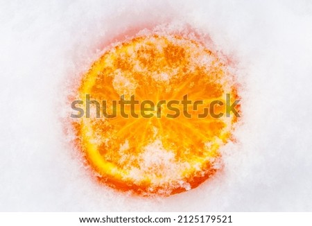 A slice of fresh frozen orange tangerine mandarin fruit cowered with white cold winter snow. Royalty-Free Stock Photo #2125179521