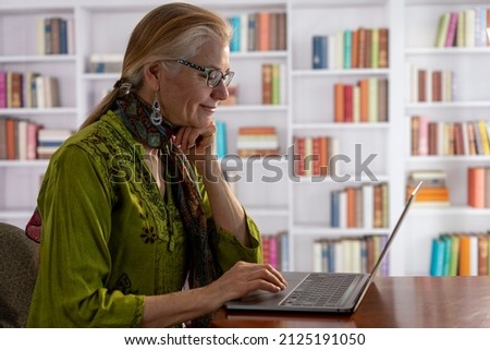 Profile of pretty, mature smiling woman working at a laptop computer in a home office library.