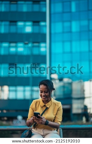 Beautiful young african american woman using a smartphone while sitting on the bench in the city