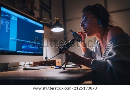 Young woman in headphones recording vocal voice using microphone with pop filter and desk top computer. Home sound studio Modern audio recording technology concept image.