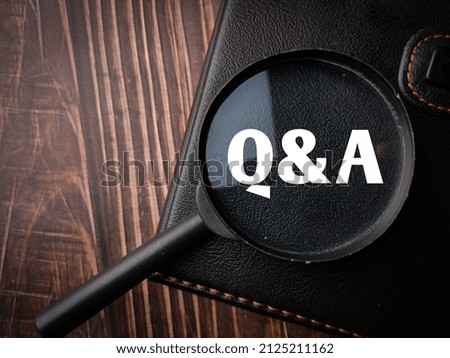 Top view magnifying glass and notebook with text Q and A on a wooden background.