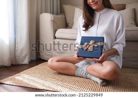 Closeup image of a young woman holding and receiving a present box at home