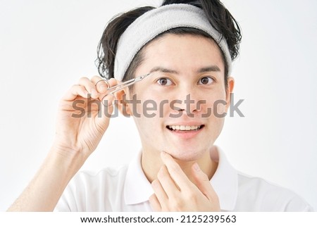 Asian man cutting their eyebrows